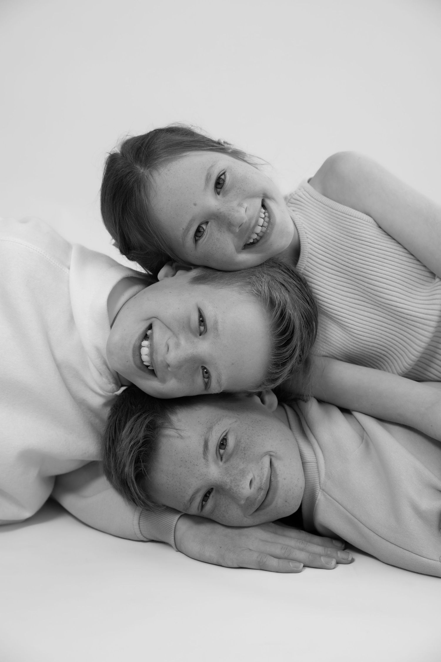 Black and white portrait of three smiling children stacked together, posing playfully for a family photo.