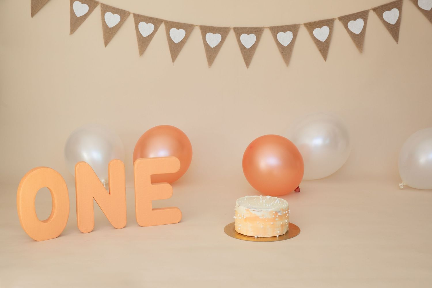 Birthday party decorations with heart bunting and peach colored balloons spelling ONE.