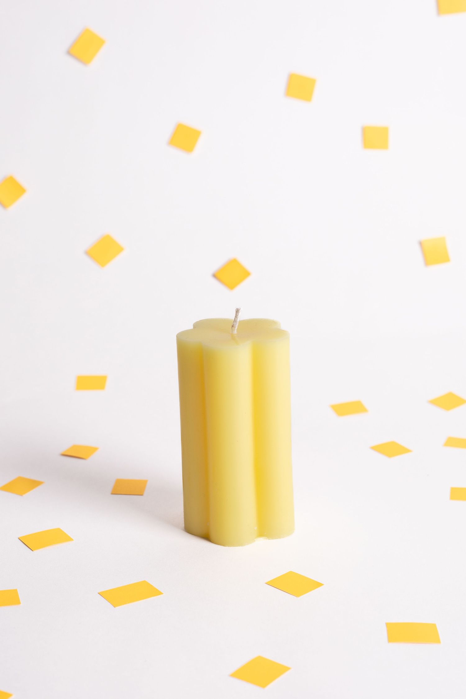 Yellow geometric candle with scattered yellow paper confetti on white background.