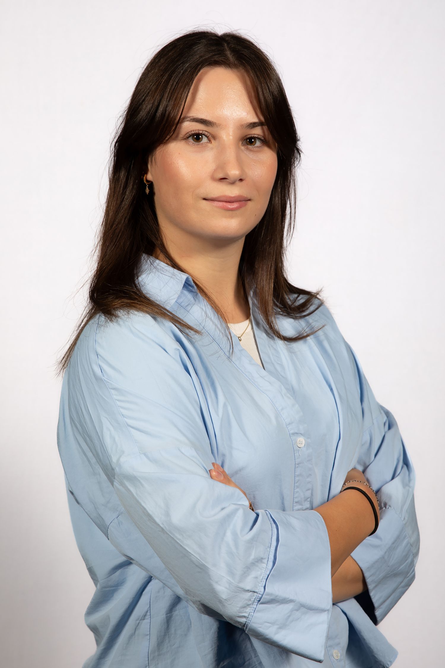 Professional wearing a light blue button-down shirt poses against white background.