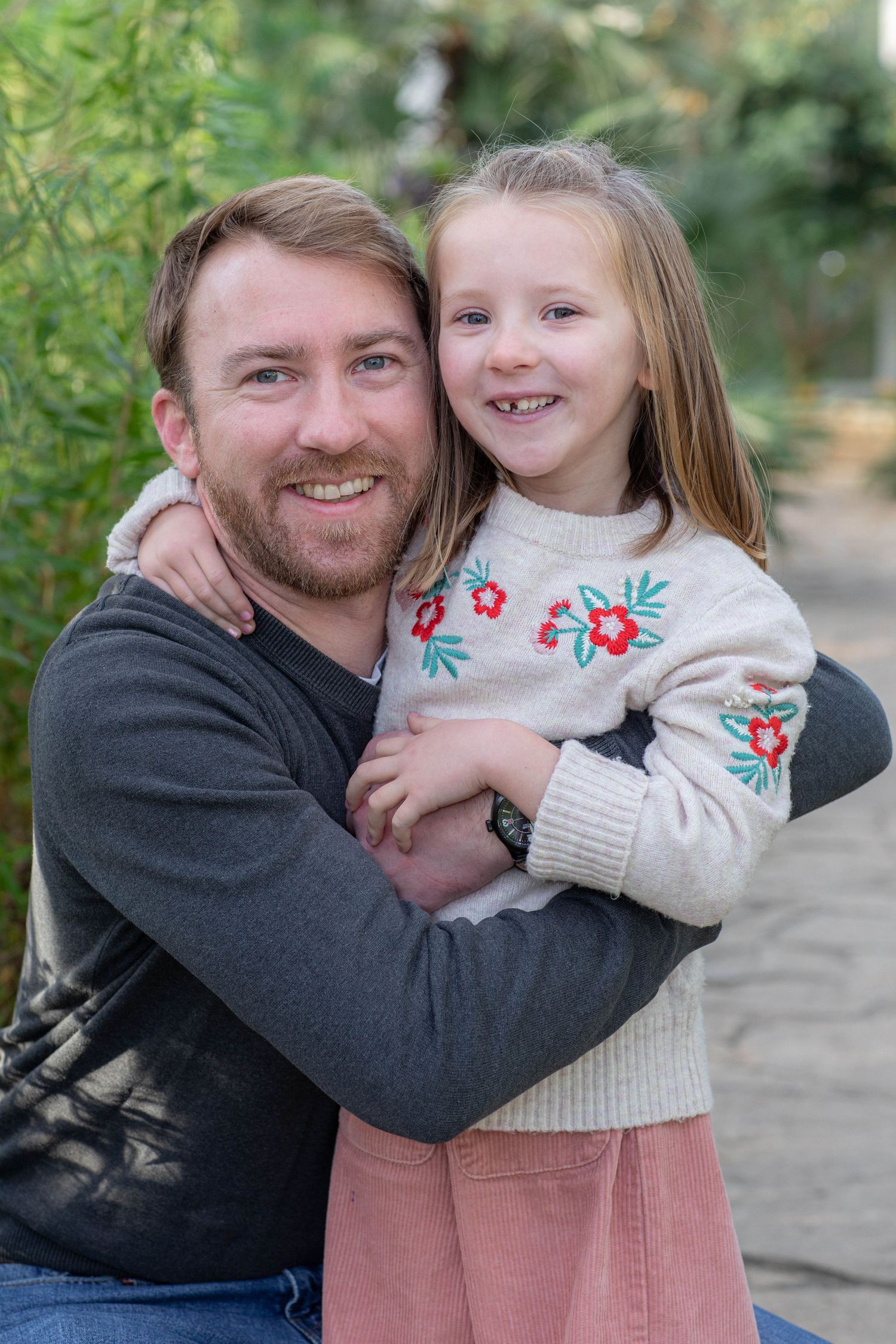 Sweet candid moment captured between parent and child hugging outdoors with natural greenery backdrop.