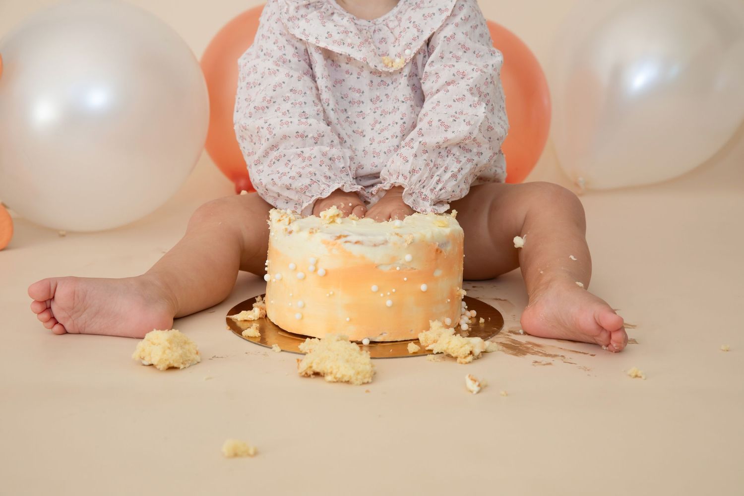 First birthday cake smash setup with orange and white balloons and scattered cake pieces.