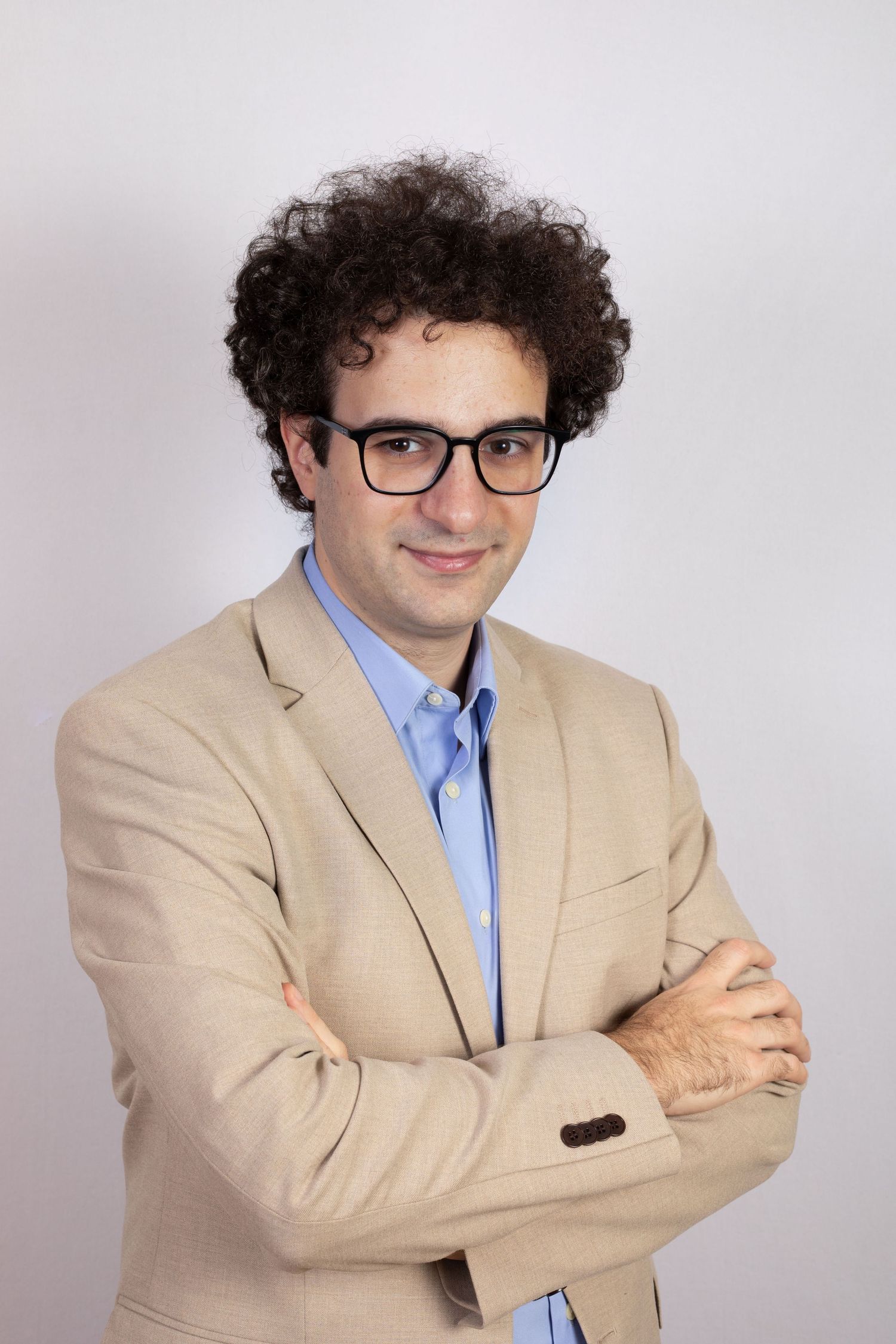 Professional in beige suit jacket and blue shirt poses against white background.