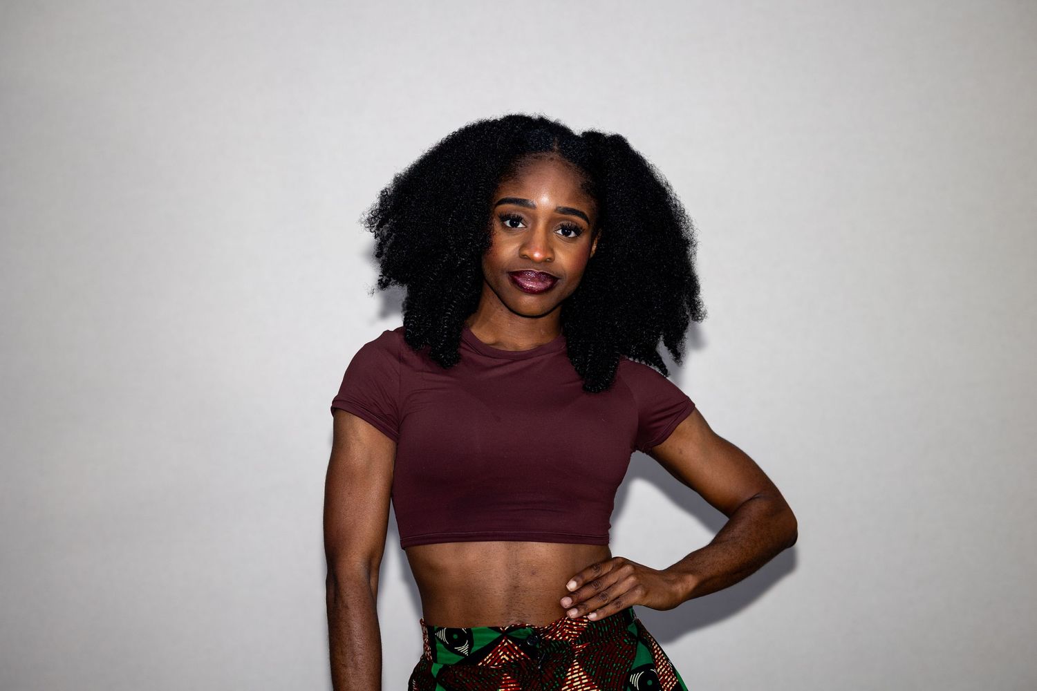 Young woman with natural afro hair in a maroon crop top and colorful skirt posing confidently.
