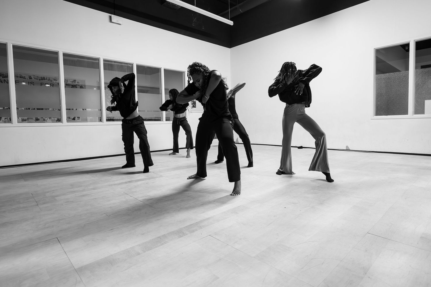 Black and white image of four dancers in dark clothing performing dynamic contemporary dance in a studio.