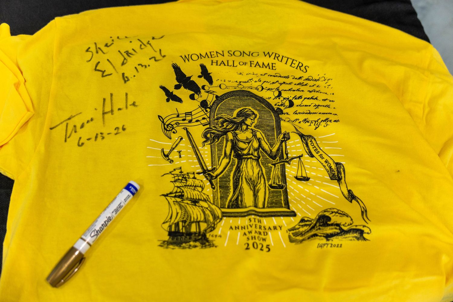Yellow Women Songwriters Hall of Fame 25th anniversary T-shirt with autographs and a gold marker on dark surface.