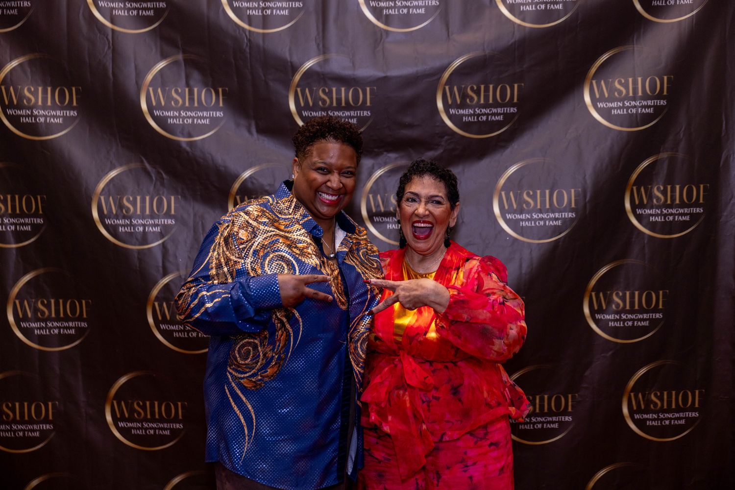 Two women pose and smile in front of a WSHOF step-and-repeat backdrop at a formal event.