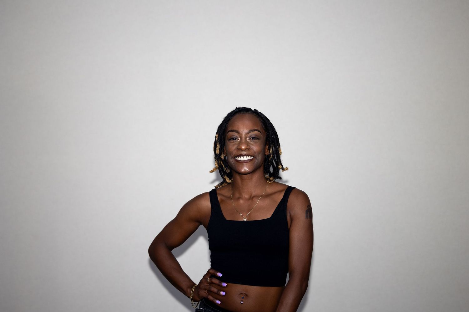 Smiling Black woman with braided hair wearing a black crop top, posing with hand on hip.