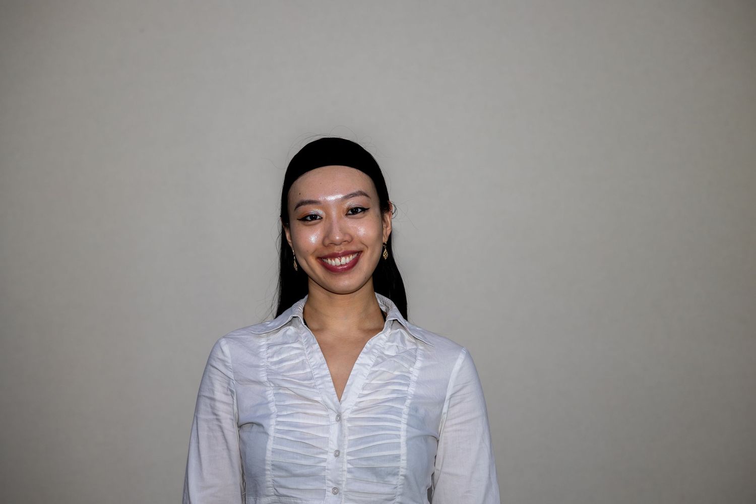 Smiling Asian woman with sleek dark hair wearing a white button-up blouse against a neutral background.