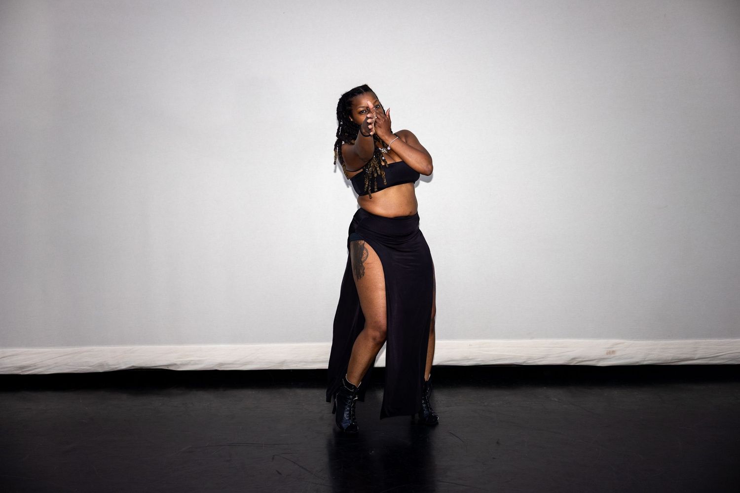 Woman in black crop top and split maxi skirt dances gracefully in a studio setting.