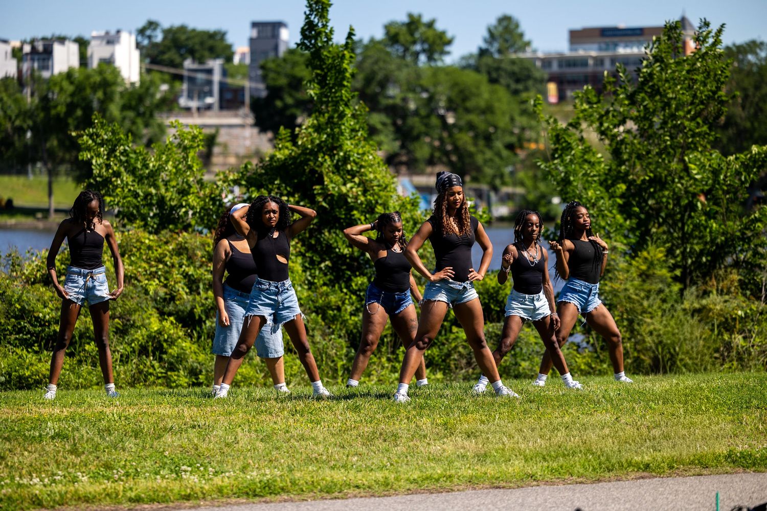 A group of young women in matching black tops and denim shorts perform a synchronized dance routine in a park.