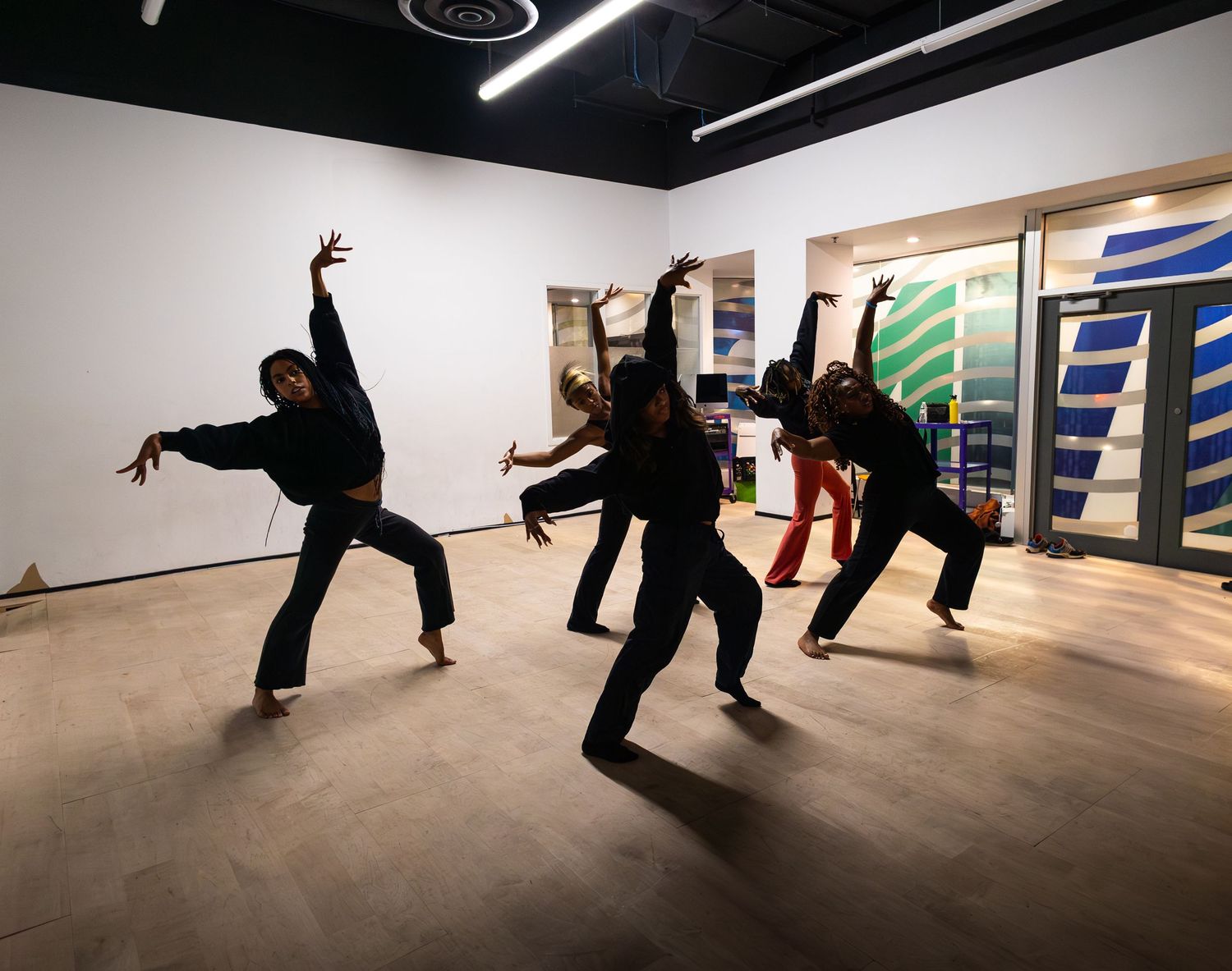 Four dancers in black outfits performing expressive contemporary dance moves in a modern studio space.