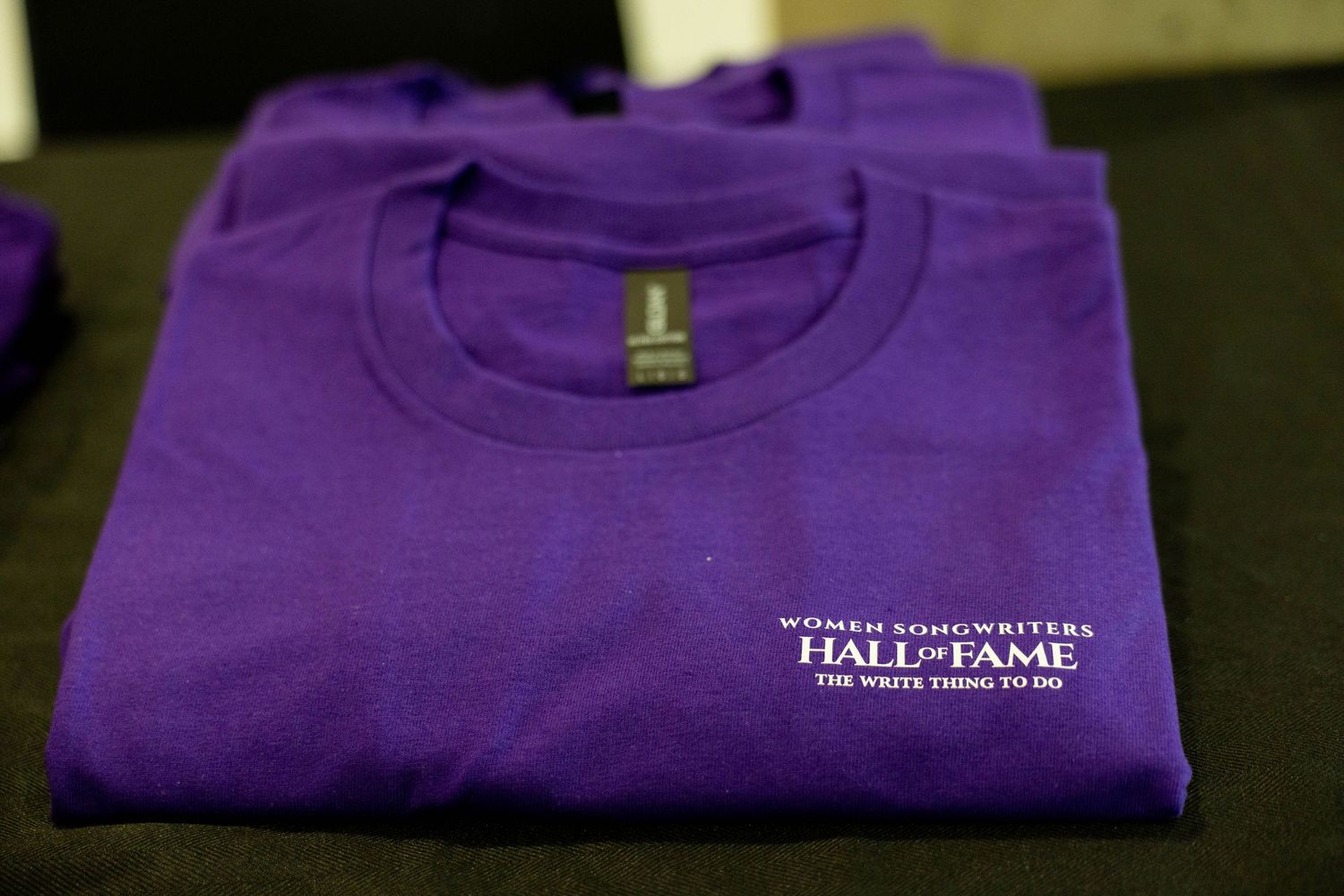 Purple Women Songwriters Hall of Fame t-shirt folded on a dark surface.