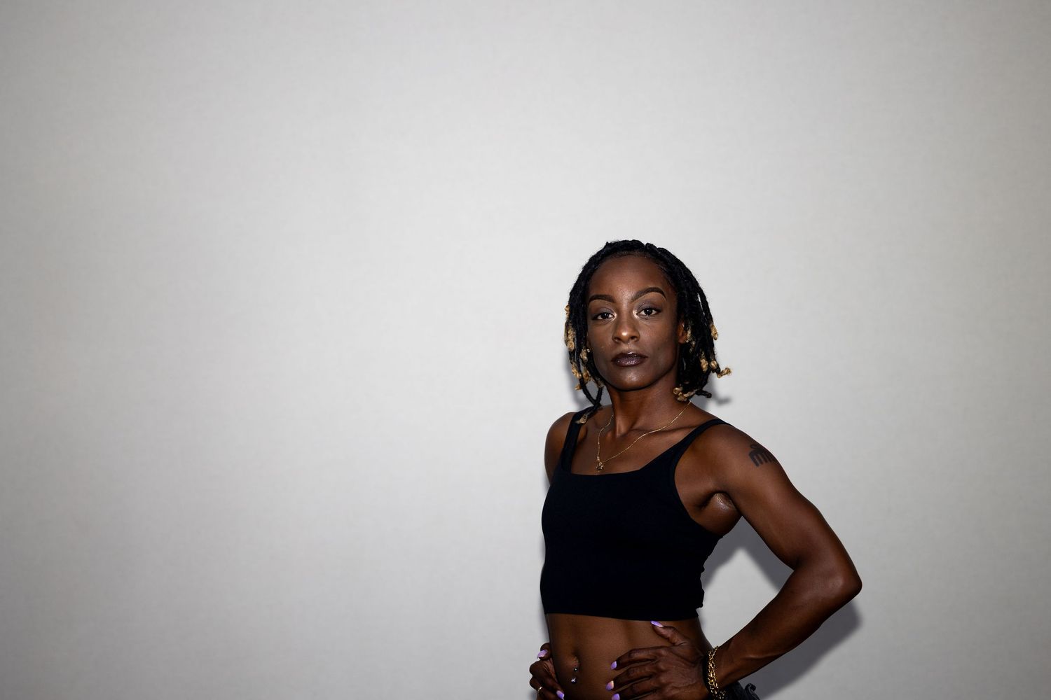 Confident young Black woman with braids in a black crop top posing with hands on hips against gray background.