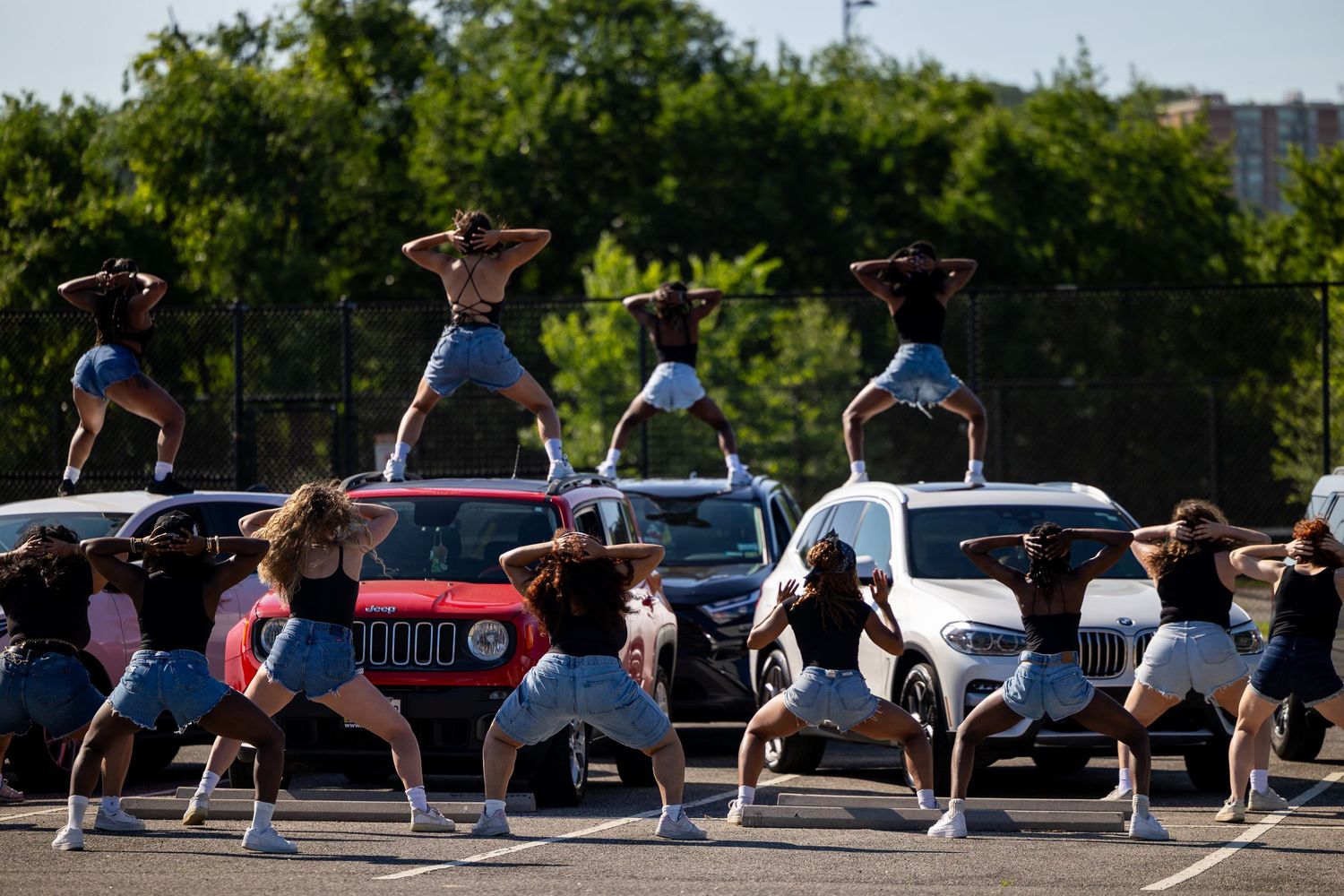 Group of dancers performing synchronized routine on cars in a sunny parking lot outdoor dance performance.