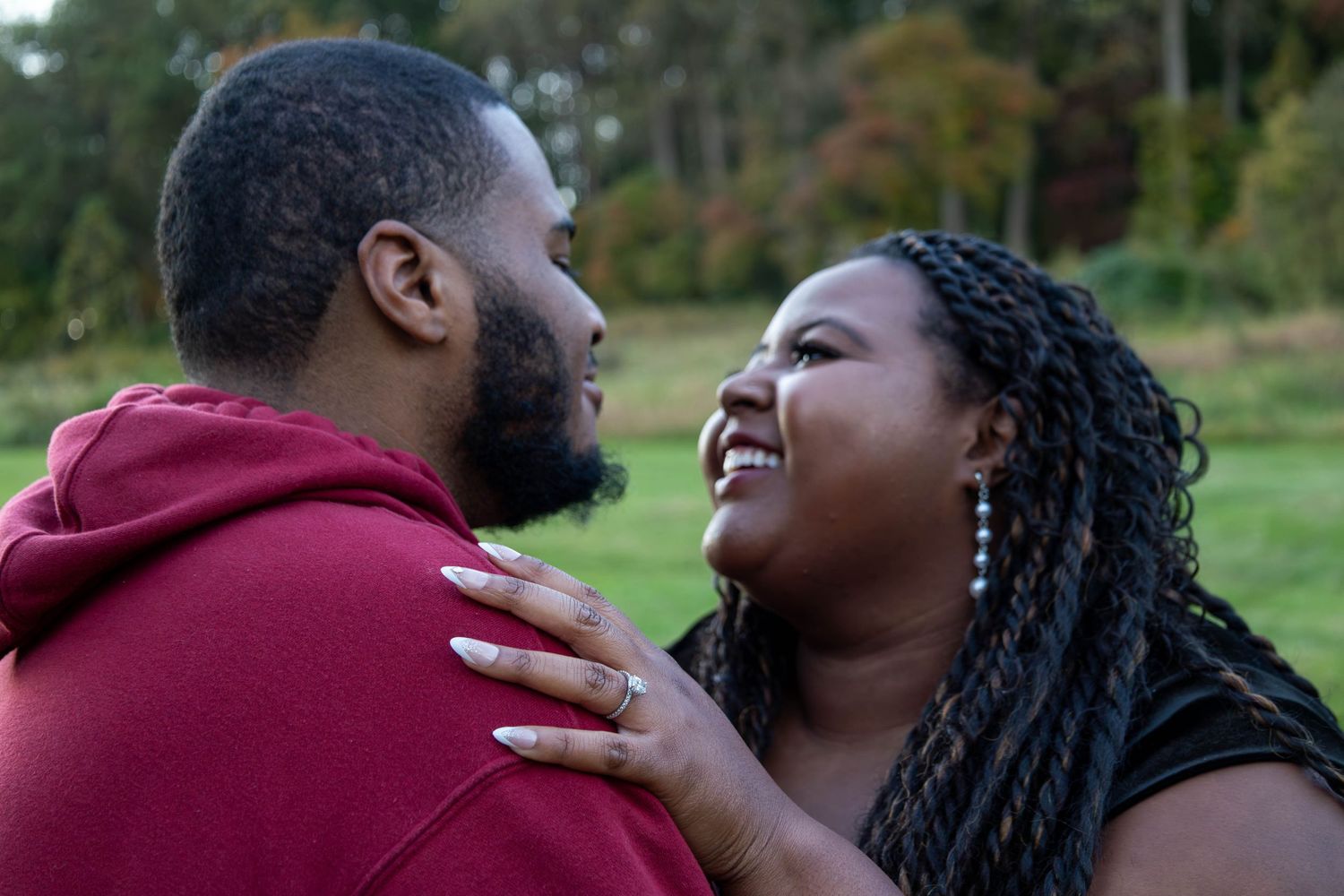 A joyful couple sharing a loving moment outdoors, woman smiling brightly while resting hands on mans chest.