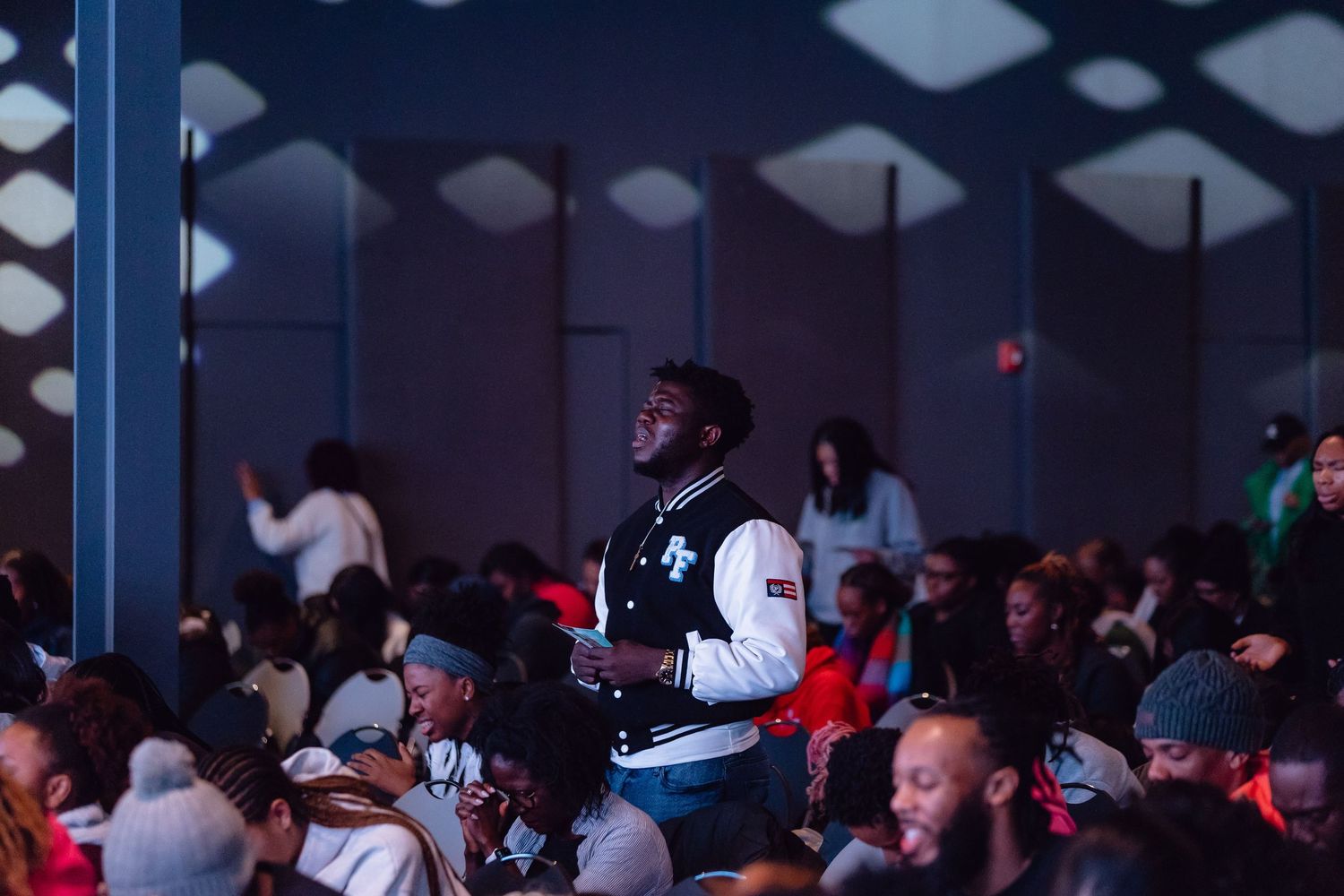 A crowded audience watches intently in a dimly lit venue during a performance or event.