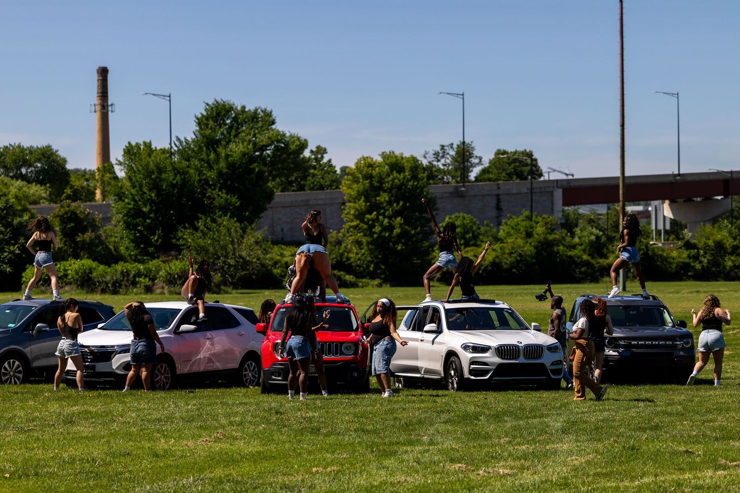 Group of people posing on and around white BMW SUVs parked on a green field during a sunny outdoor event.