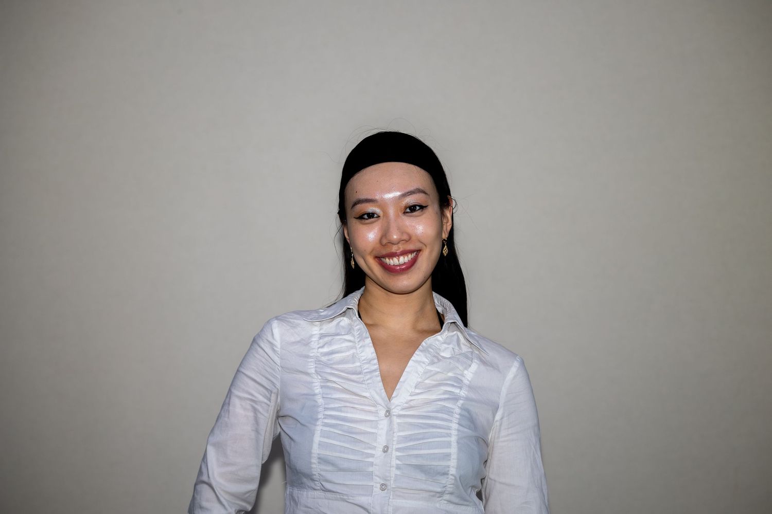 Smiling woman in white button-up shirt with dark headband poses against neutral background.