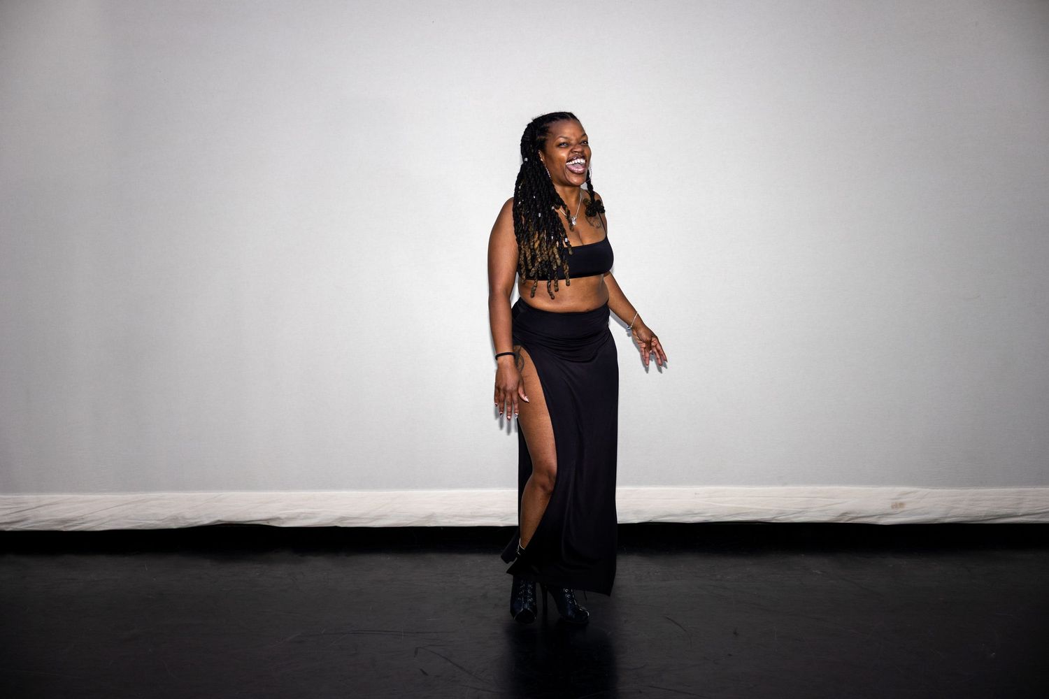 Woman in black fringe skirt and crop top smiling in a studio.