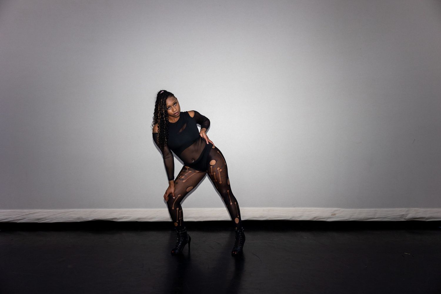 Dancer in black fishnet outfit striking a dynamic pose in a professional studio setting.