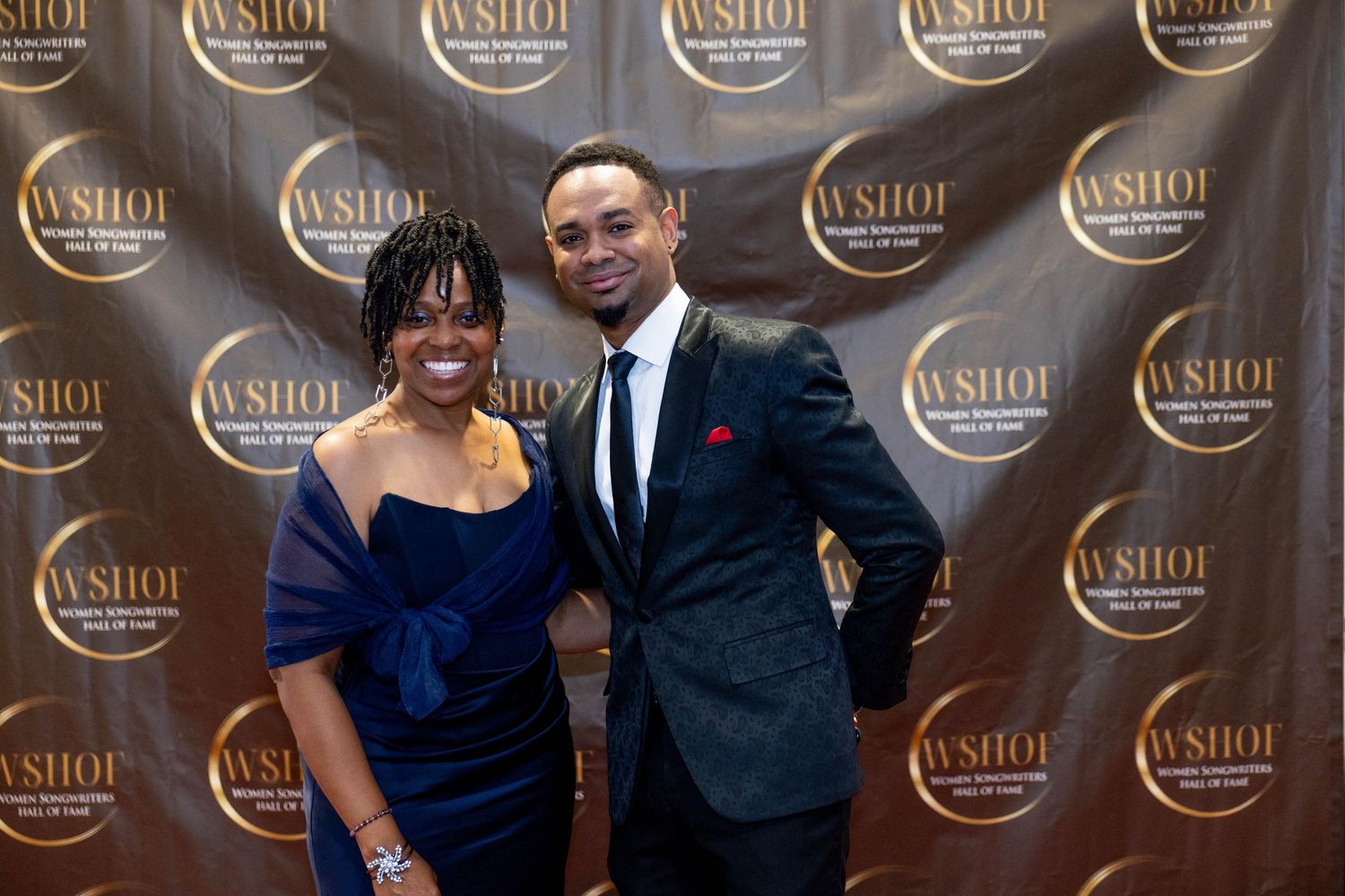 Two elegantly dressed attendees pose together at a WSHOI awards event backdrop.