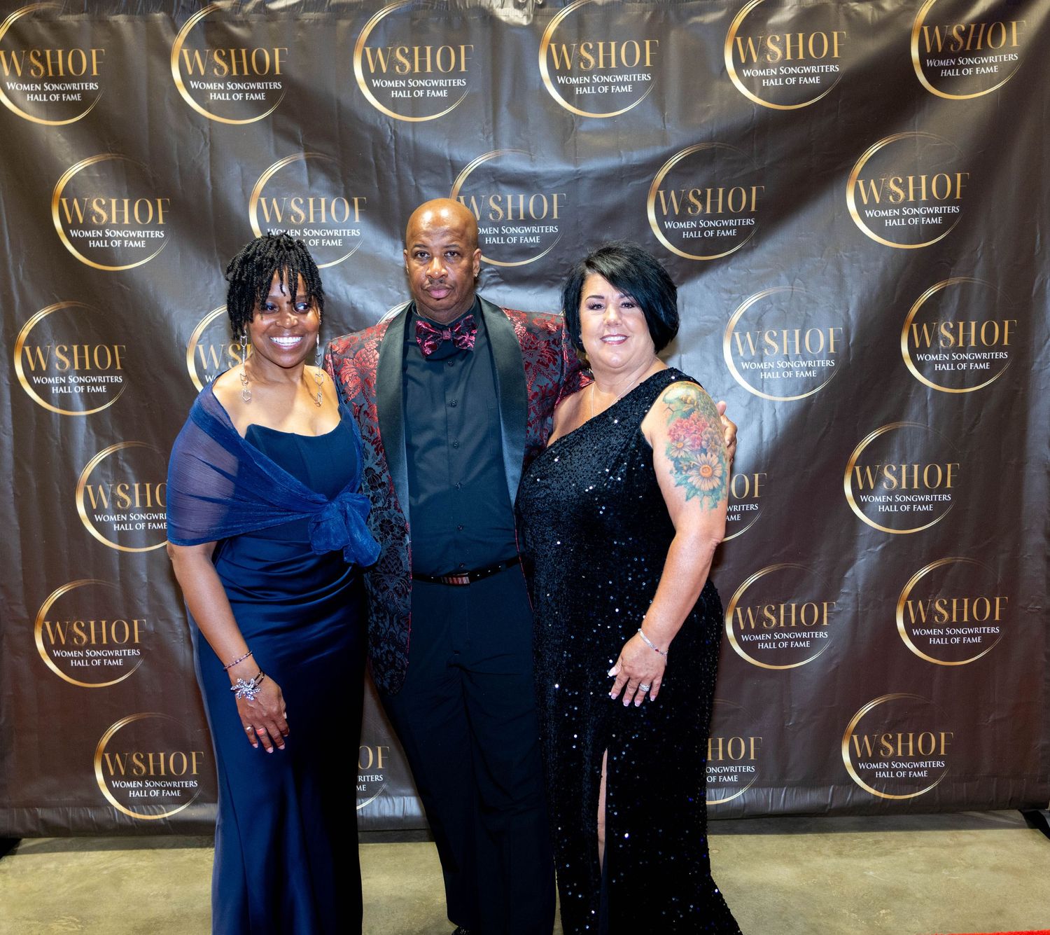 Three people posing together at a WSHOF awards event backdrop, dressed in elegant formal attire.