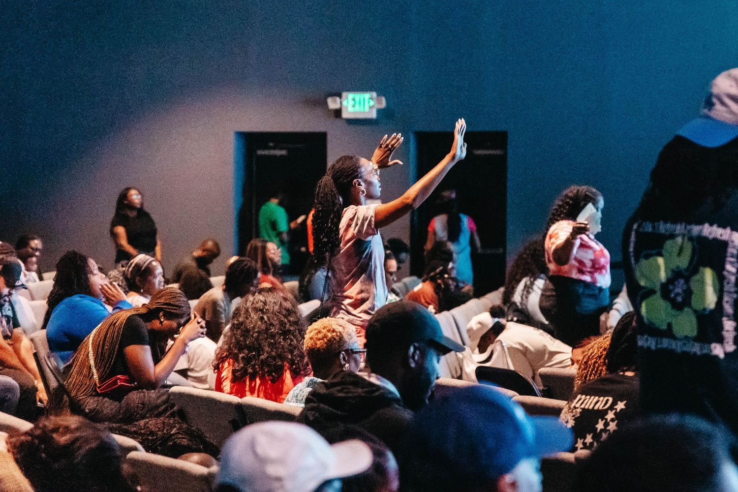 Audience members raising hands during an indoor event with dramatic lighting.