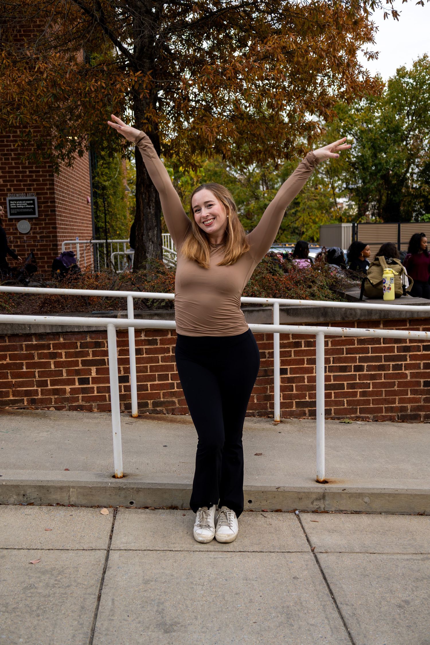 Person in casual attire strikes energetic poses near white railing during autumn photoshoot.