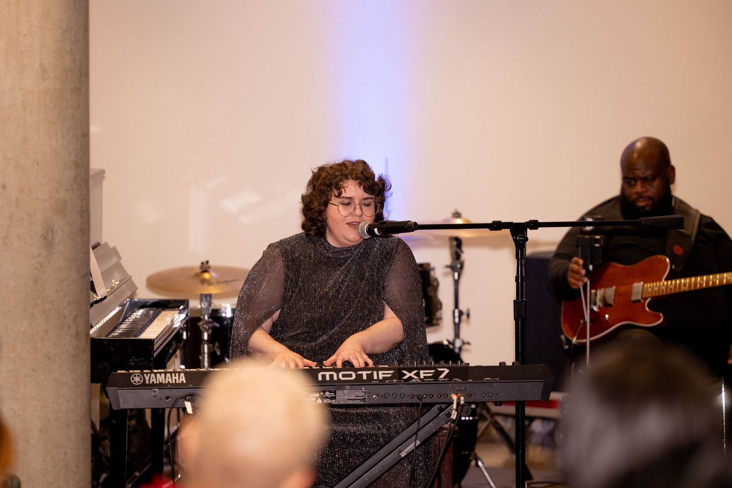 Musician plays Yamaha keyboard with guitarist performing live at an indoor event.