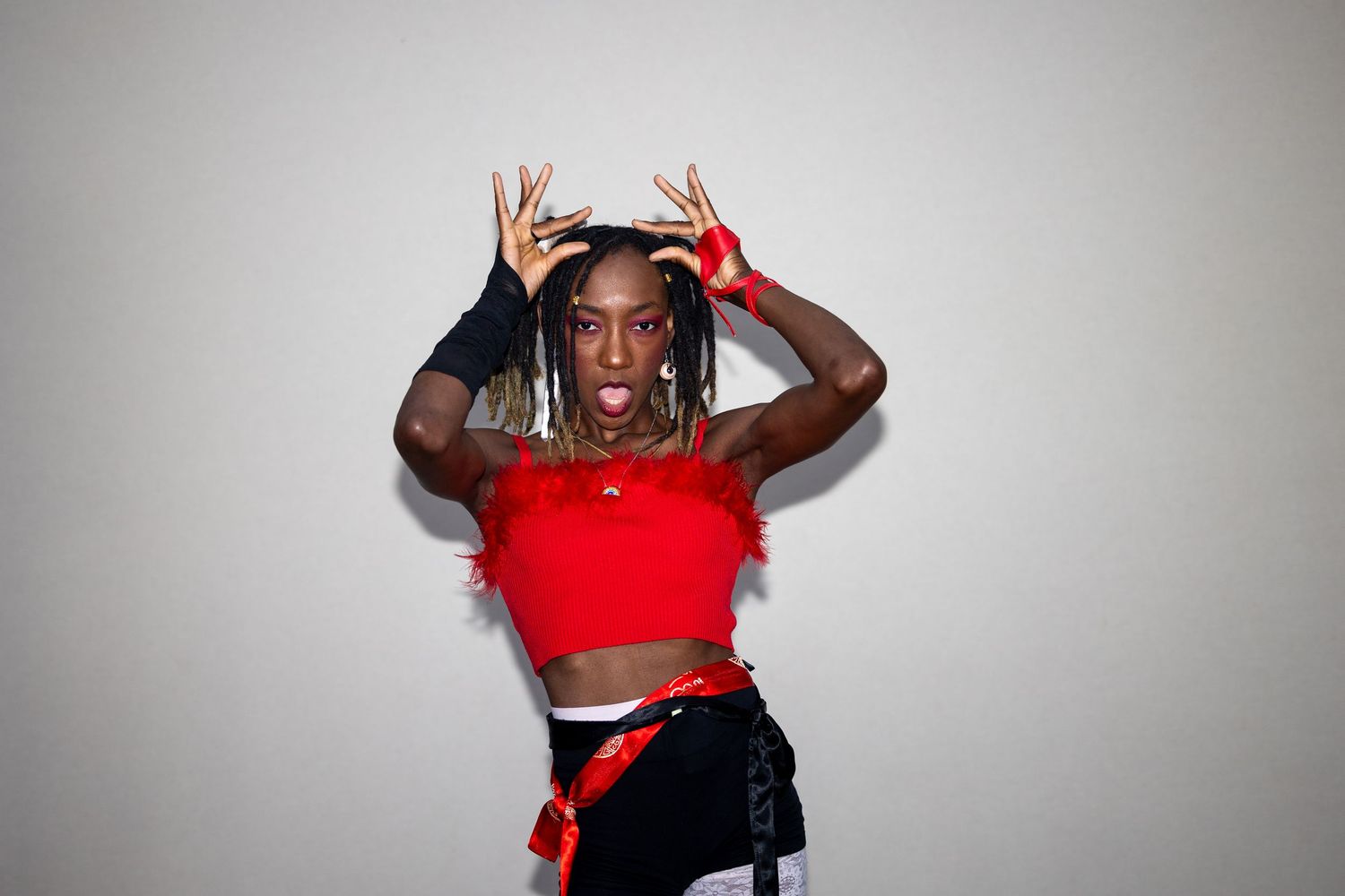 Energetic performer in red crop top making antler gestures with hands while wearing black gloves and accessories.