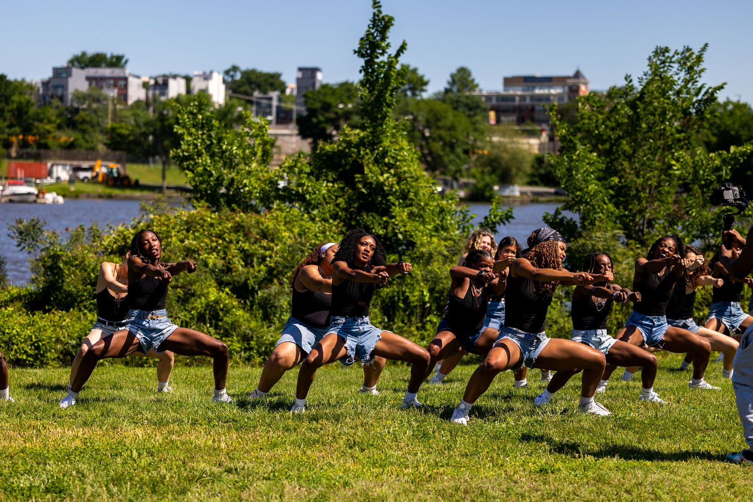 Group of performers doing a traditional Maori haka dance outdoors near a river on a sunny day.