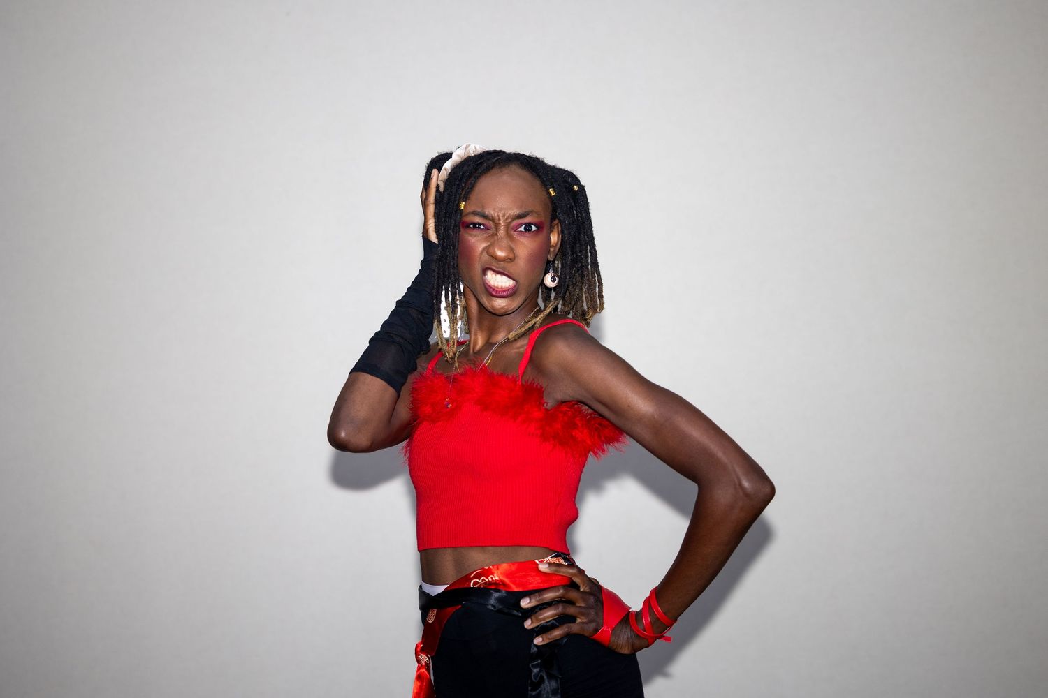 Confident Black woman in red crop top and black gloves striking a pose against a white background.