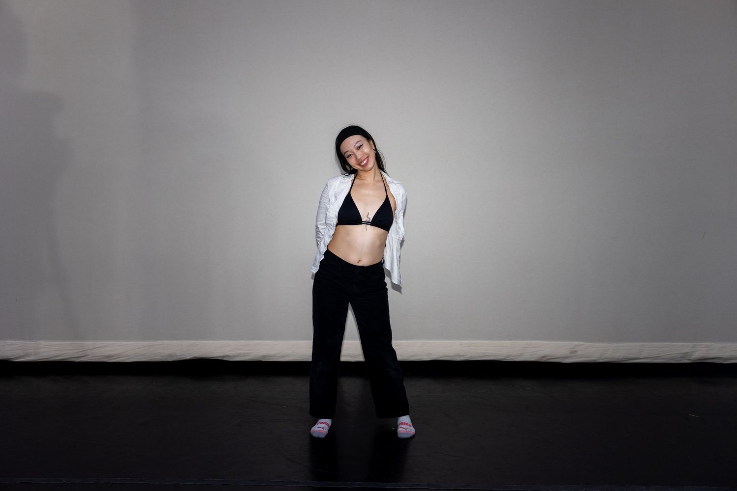 Woman in black bralette and wide-leg pants with white blazer striking a pose in studio.