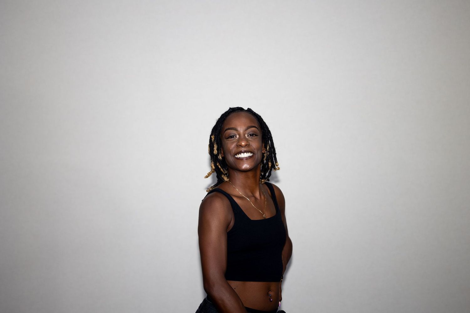 A slender woman with braids wearing a black crop top laughs joyfully against a plain white background.