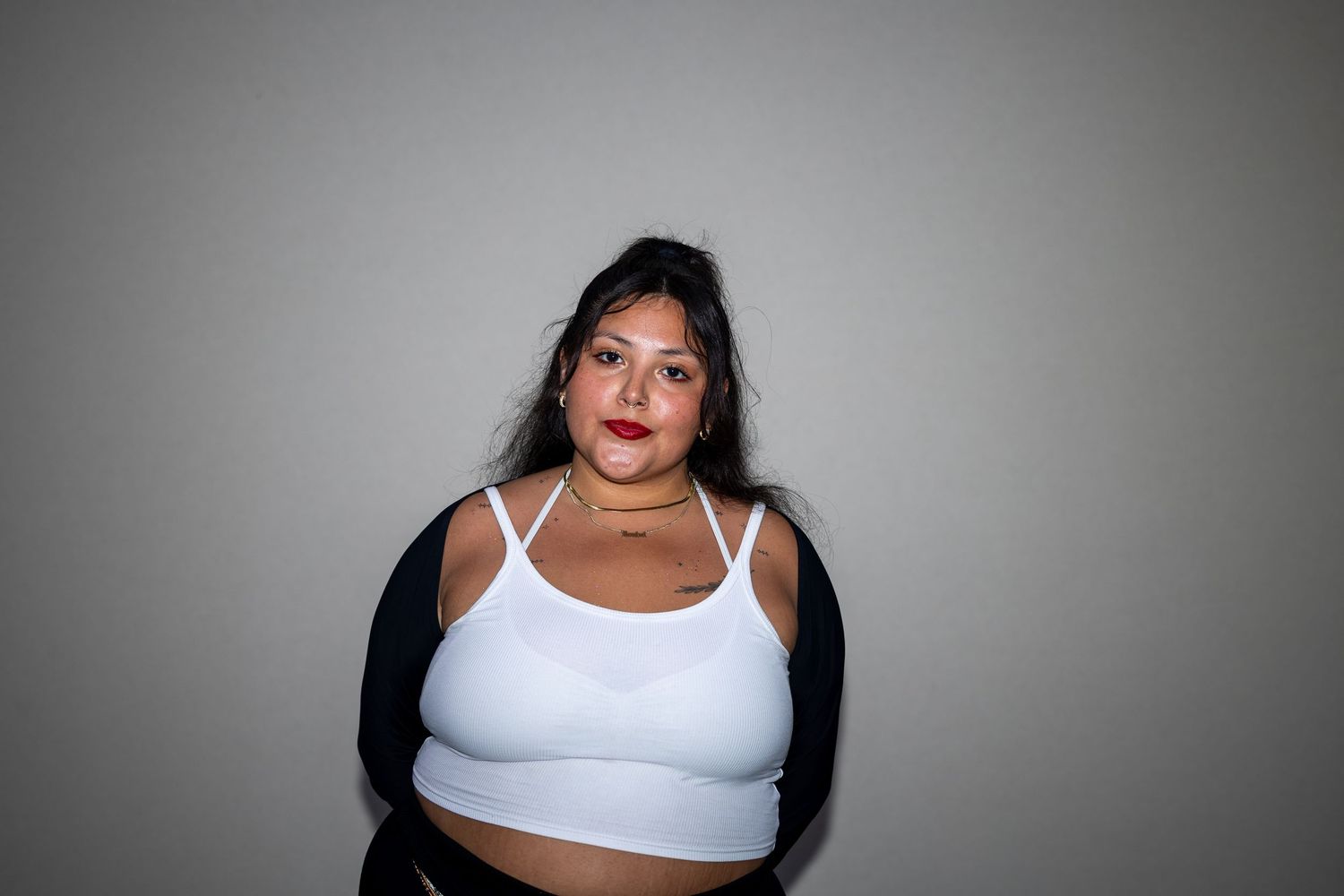 Woman in white bralette and black cardigan poses against gray background.