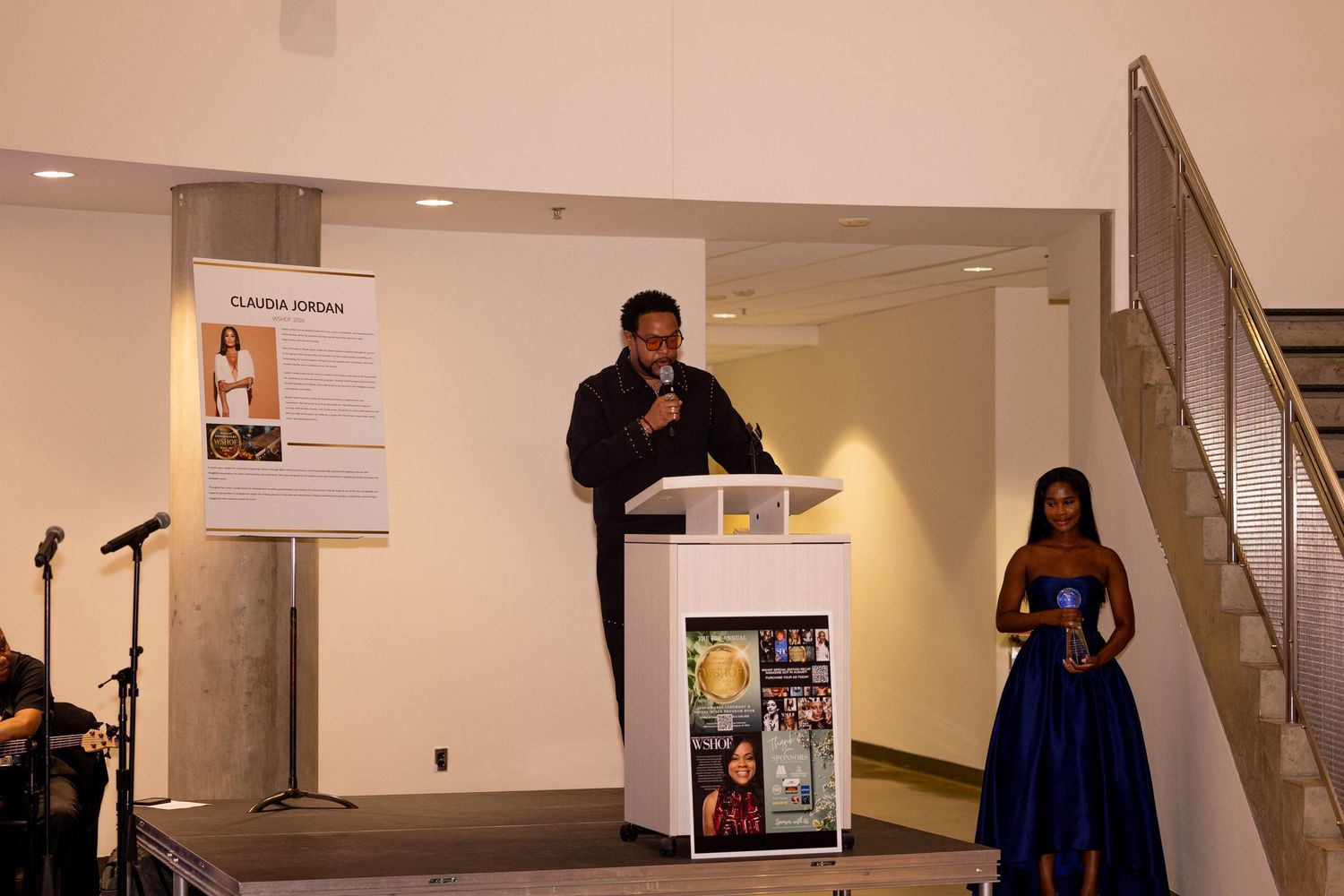Man speaking at podium during Claudia Jordan event with woman in blue gown.