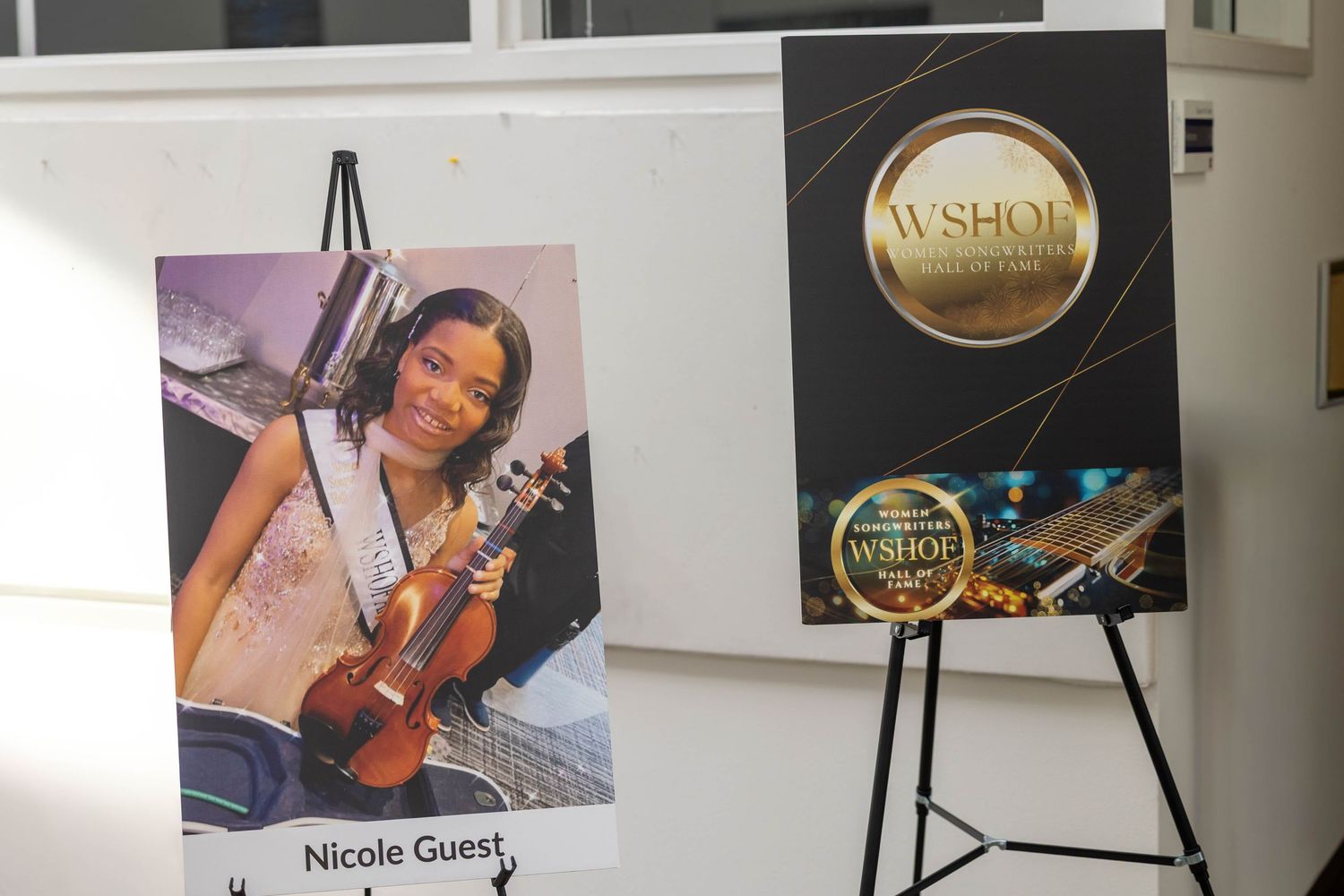 Nicole Guest poses with her violin next to WSHOF award plaques displayed on easels at a ceremony.
