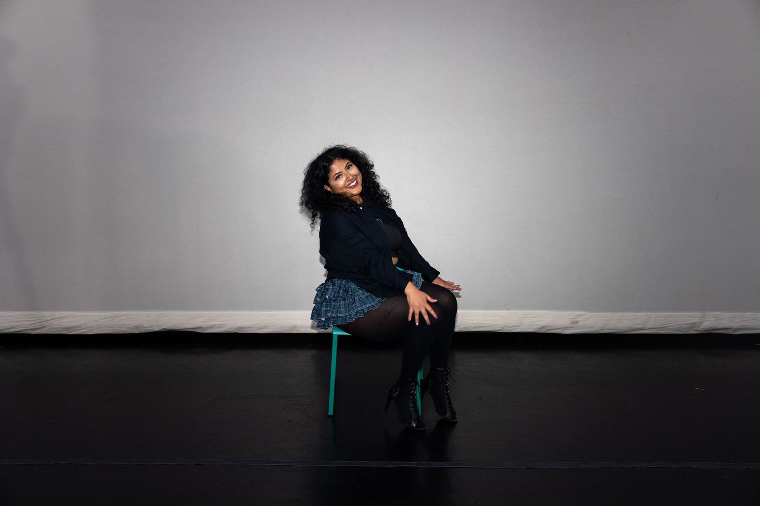 Woman in blue skirt sitting gracefully on a stool in a professional photo studio.
