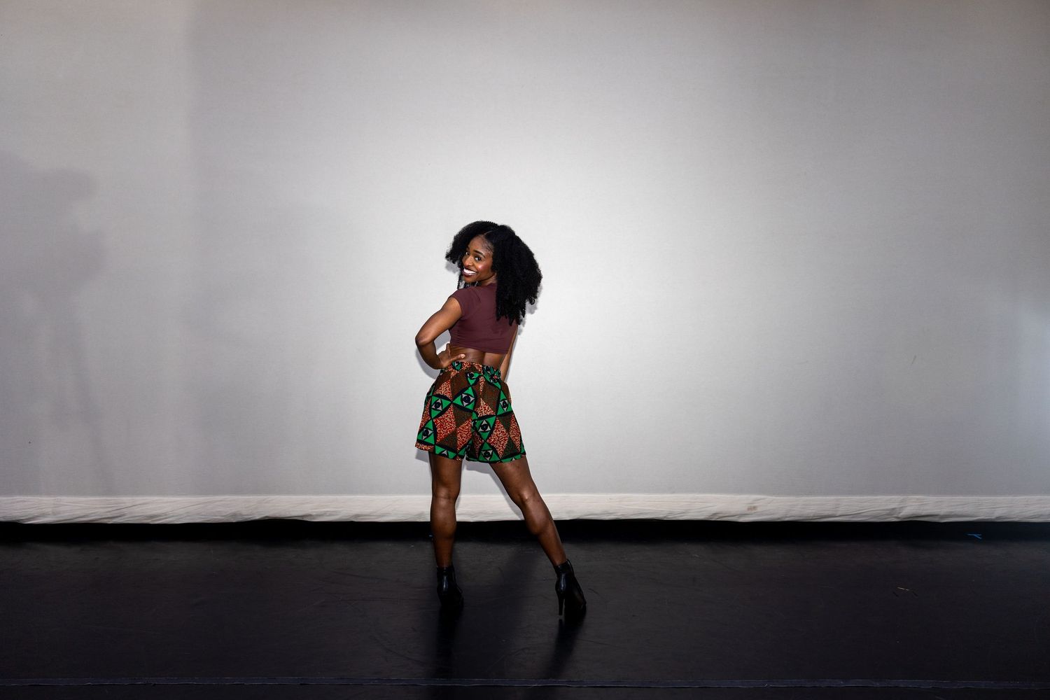 A dancer in a vibrant African print skirt and crop top performs a graceful turn on stage.