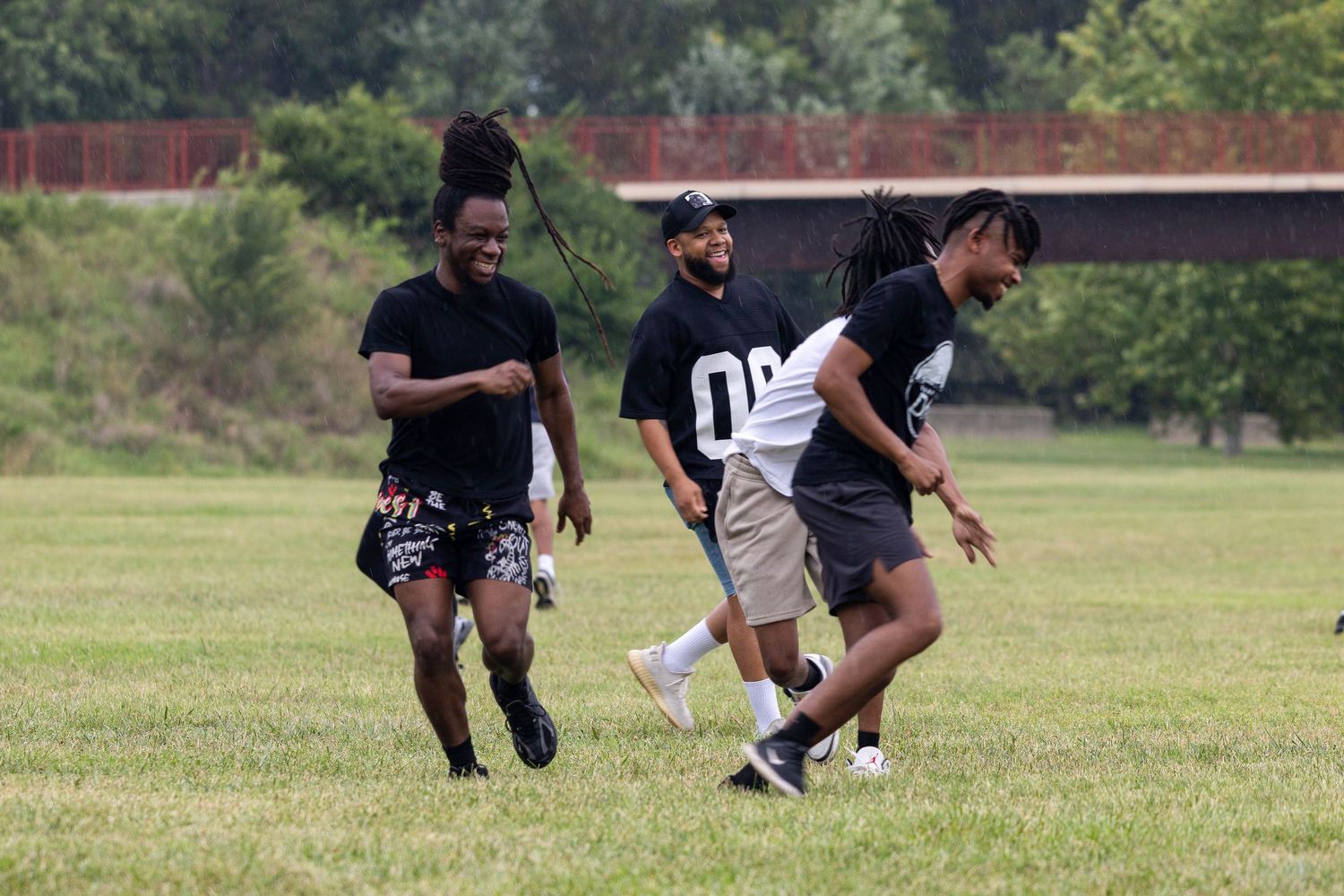 Three young men in black shirts jogging and laughing together on a green grass field.