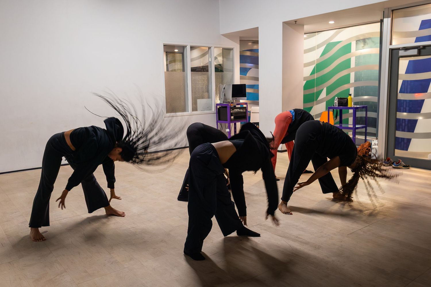 Dancers in black attire perform dynamic movements in a gallery space with colorful wall art.