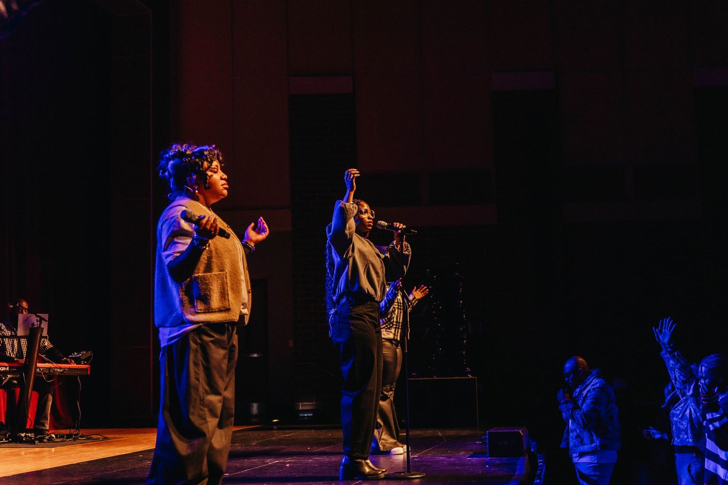 Performers on stage in silhouette against dramatic blue and orange lighting during a theatrical production.