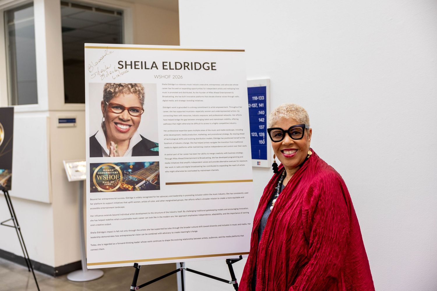 Sheila Eldridge stands beside her inductee display board at the WSHOF Hall of Fame ceremony.