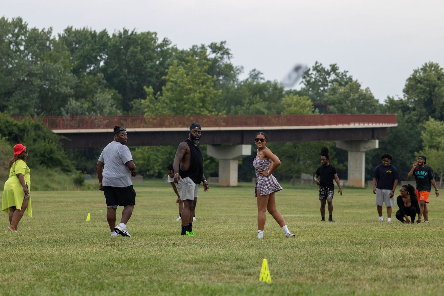 Group of people participating in outdoor sports training drills on a grass field with orange cones marking the course.