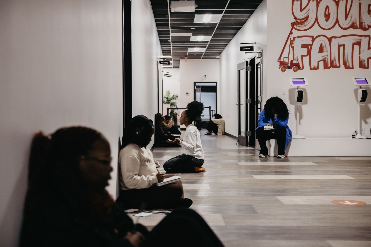 Minimalist interior hallway with white walls and black ceiling tiles showing silhouettes of people walking.