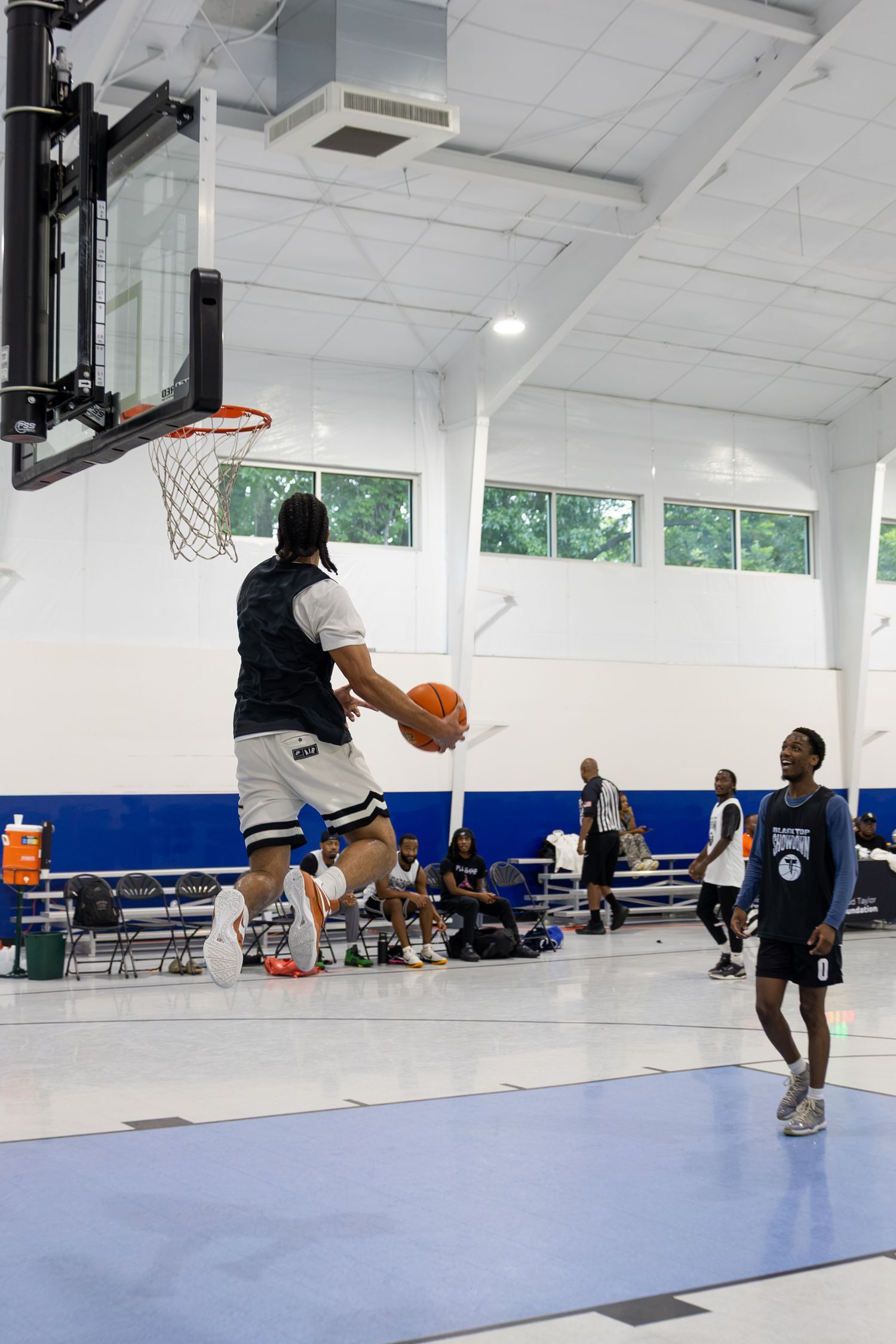 A basketball player leaps toward the hoop for a layup during an indoor recreational game while teammates watch nearby.