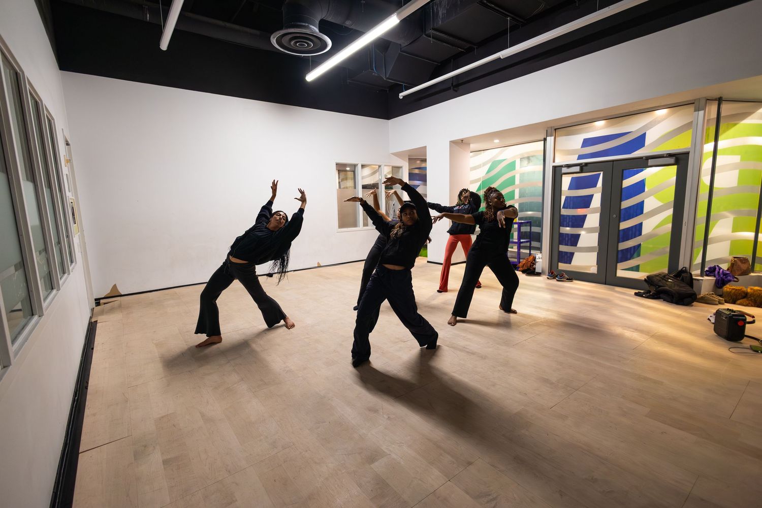 Group of dancers in black outfits practicing dynamic moves in a modern studio with wood floors.