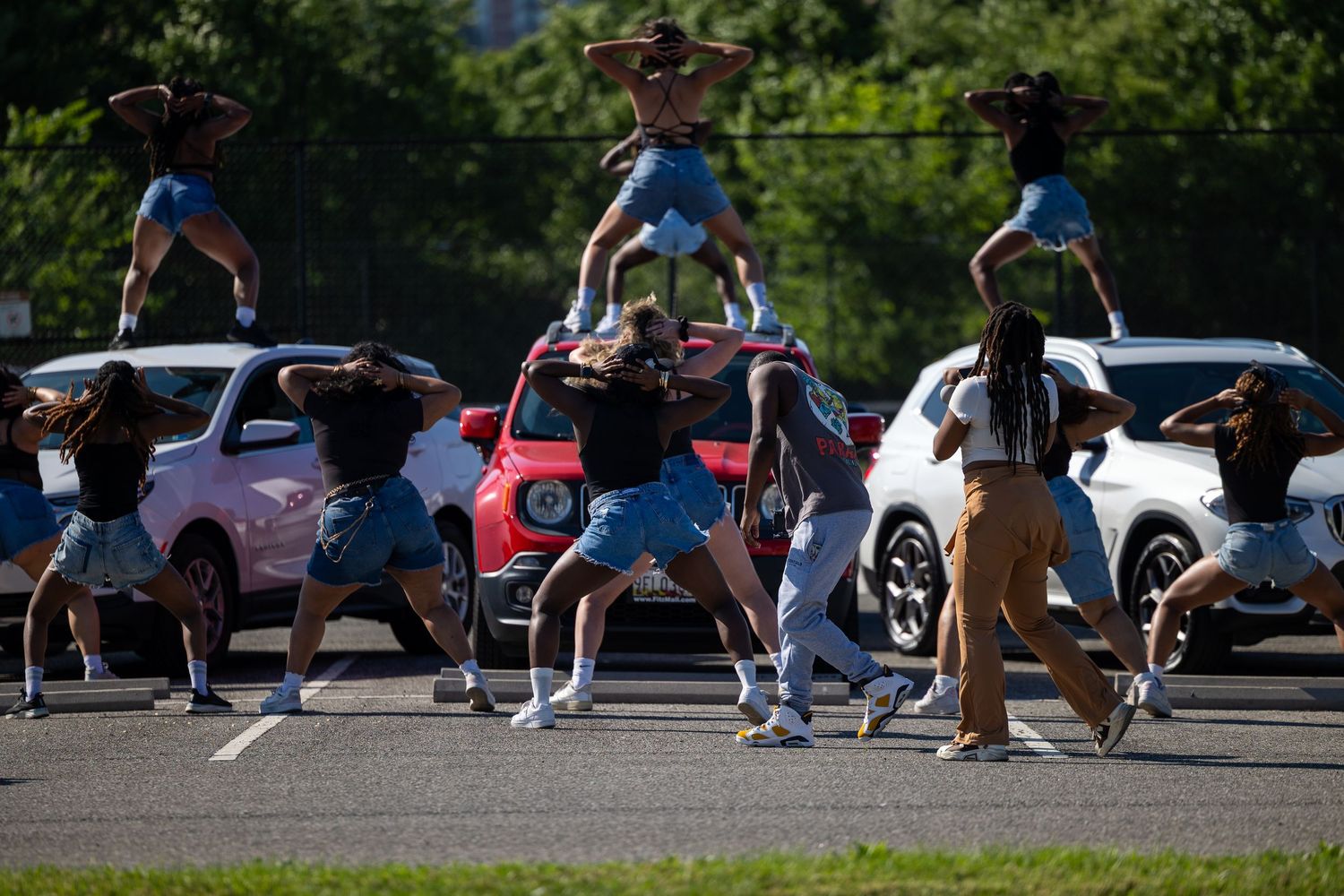 A dance team performs a synchronized routine in a parking lot, forming a human pyramid atop a car.