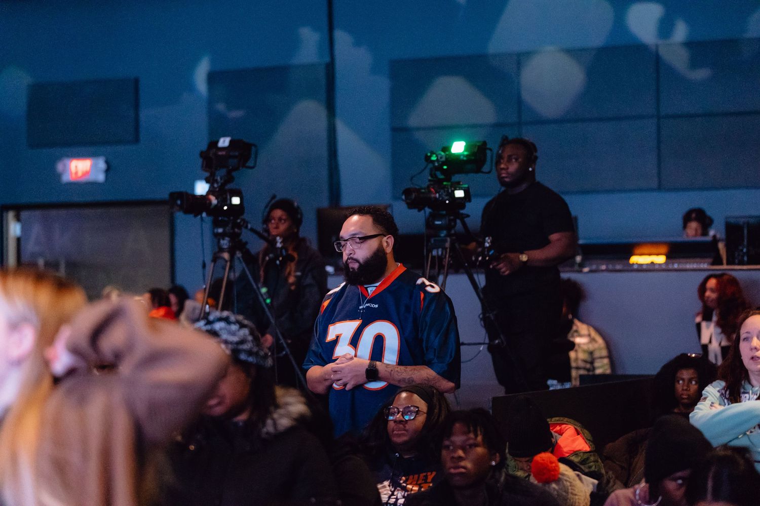 A crowded esports tournament venue with spectators watching competitive gaming on large screens in a dark arena.